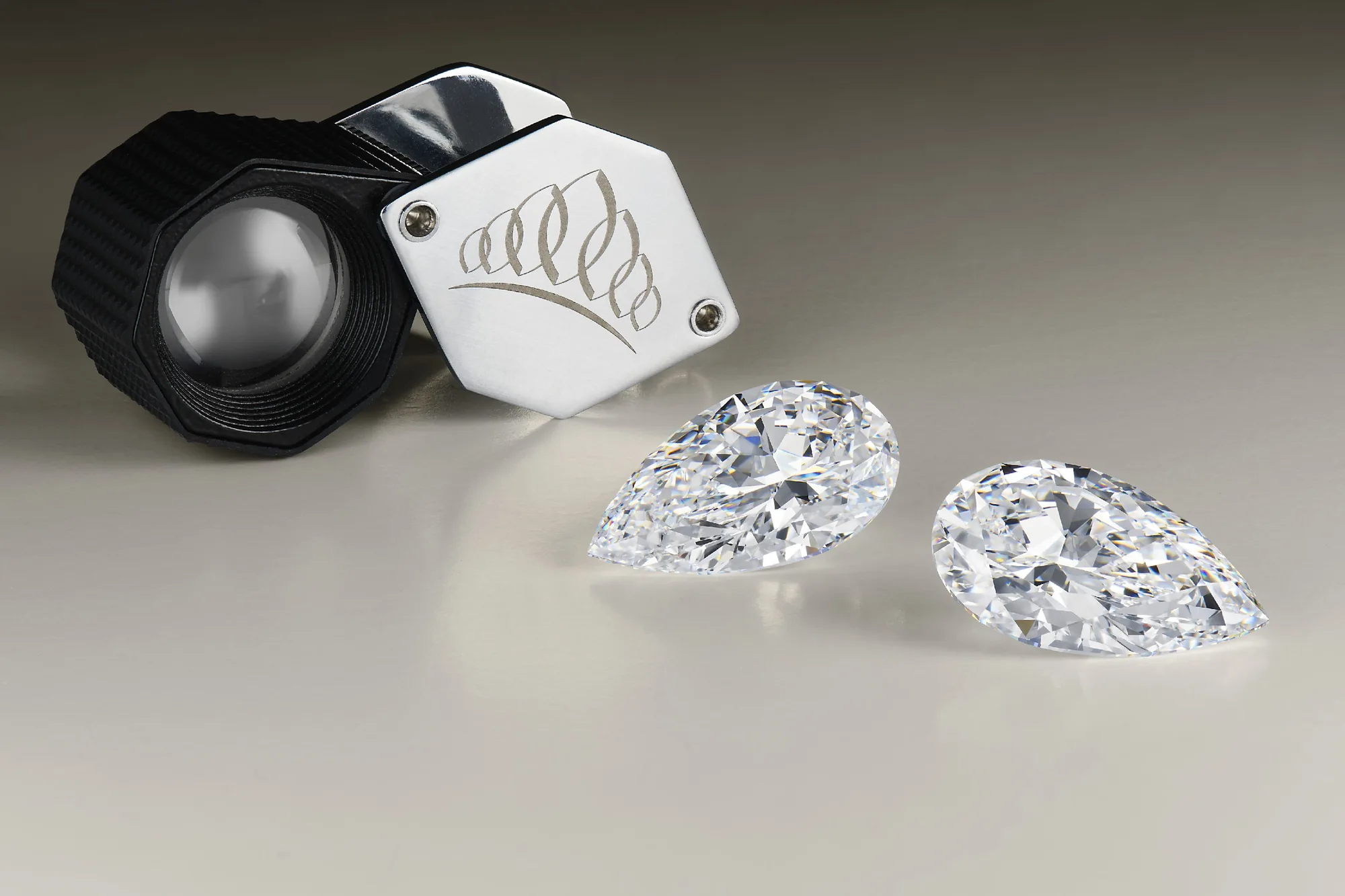 A Kwiat loupe beside two exceptionally large pear-shaped diamonds