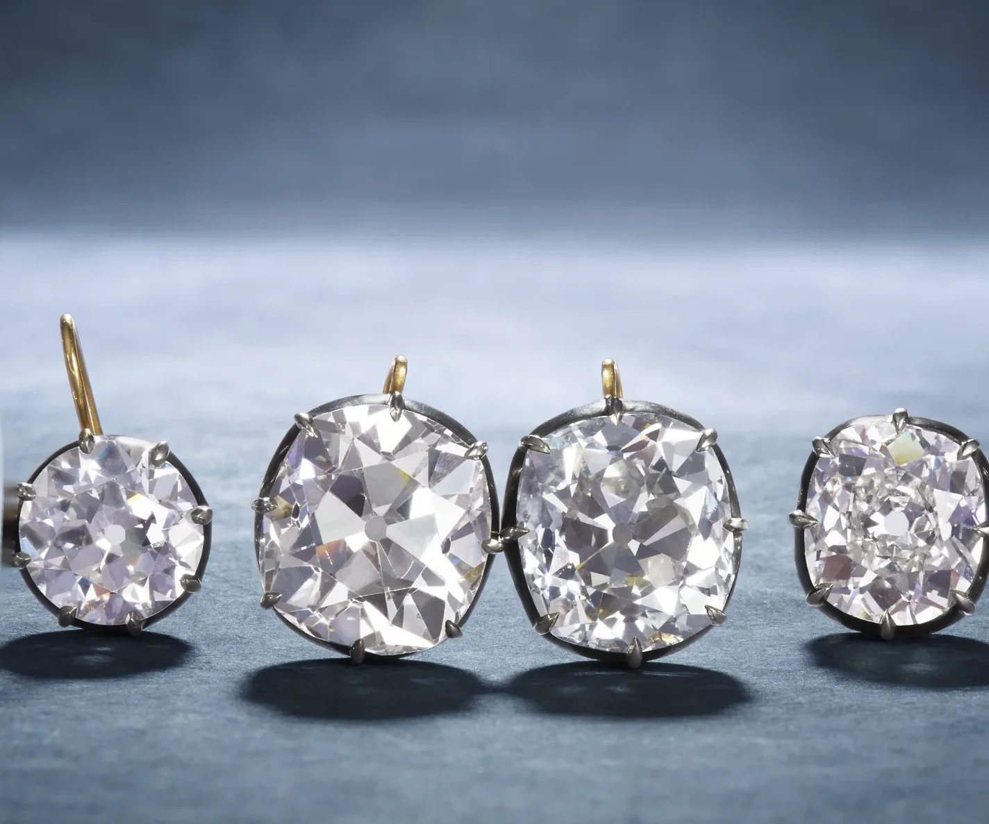 Four exceptional antique diamond earrings on a blue-gray surface